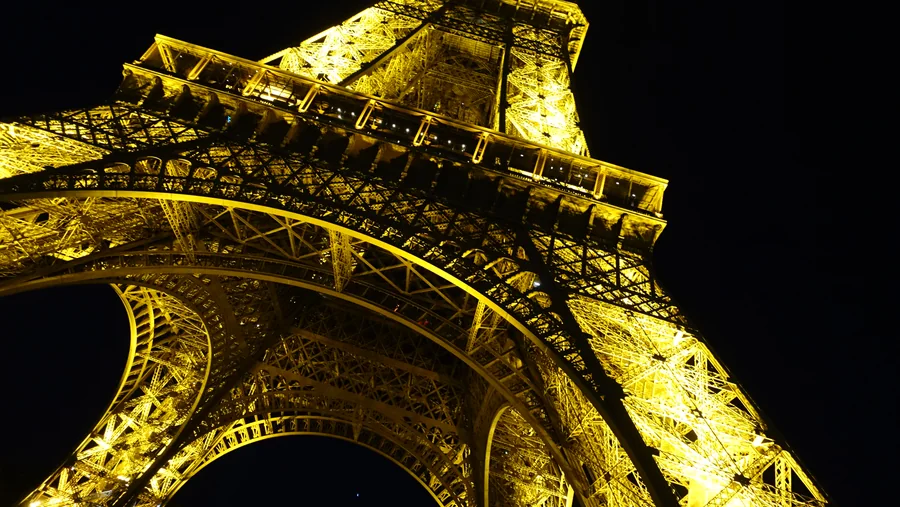 A low-angle view of the Eiffel Tower glowing gold against the night sky.