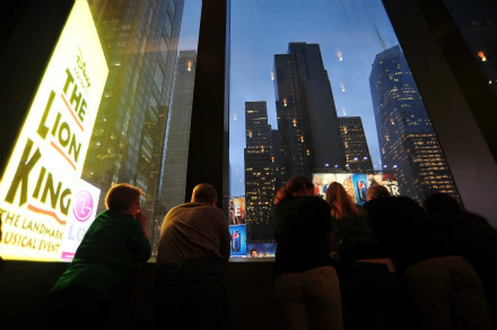 People silhouetted against a window overlooking Times Square at dusk.