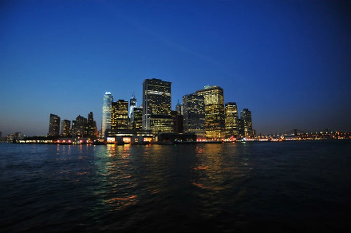 An illuminated waterfront skyline reflected beneath a deep blue evening sky.