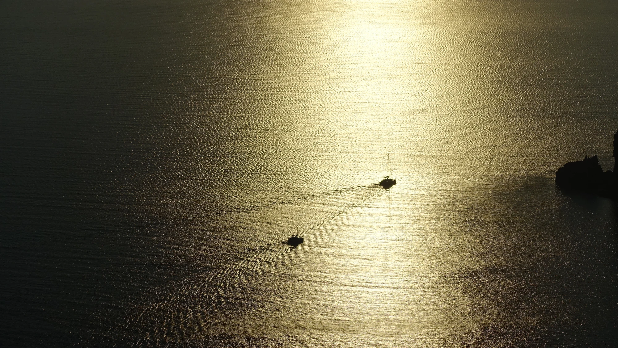 Two small boats leave curved wakes across a sunlit golden sea.